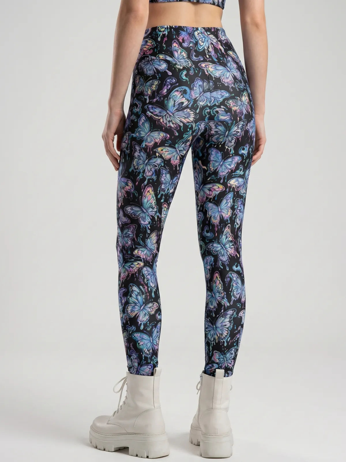 Back view of form-fitting High Waist Festival Pants featuring a neon blue and purple butterfly pattern on a black background.