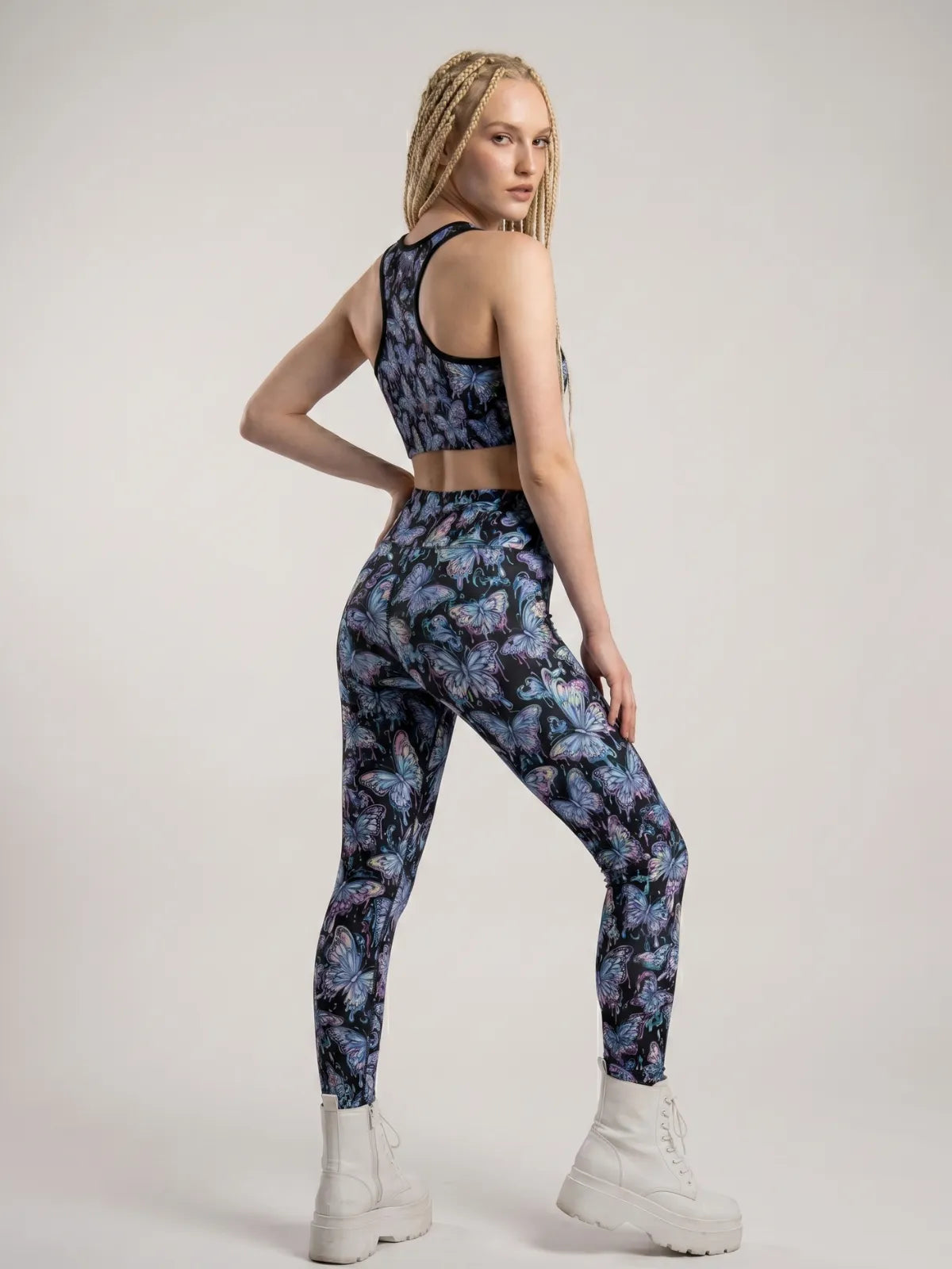 Model looking over her shoulder wearing Butterfly Rave Leggings with a vibrant psychedelic print, styled with a matching crop top and white platform boots.