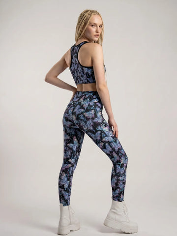 Model looking over her shoulder wearing Butterfly Rave Leggings with a vibrant psychedelic print, styled with a matching crop top and white platform boots.