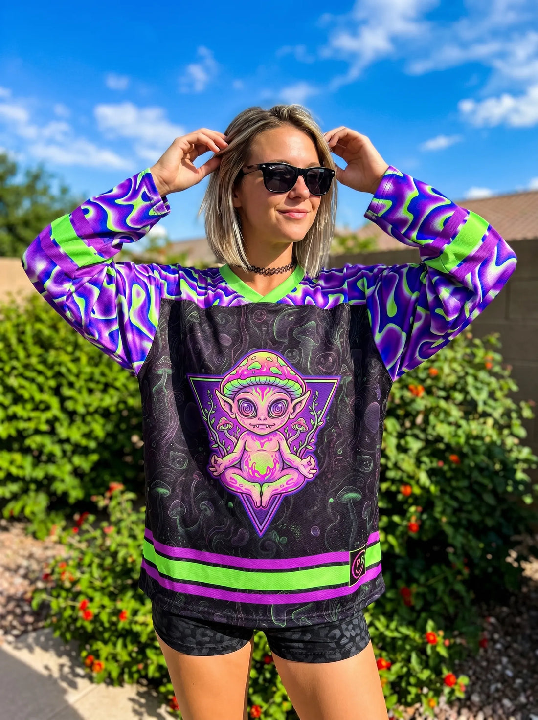Woman outdoors wearing a black oversized rave hockey jersey featuring a neon green and purple trippy alien mushroom graphic and wavy liquid sleeve patterns